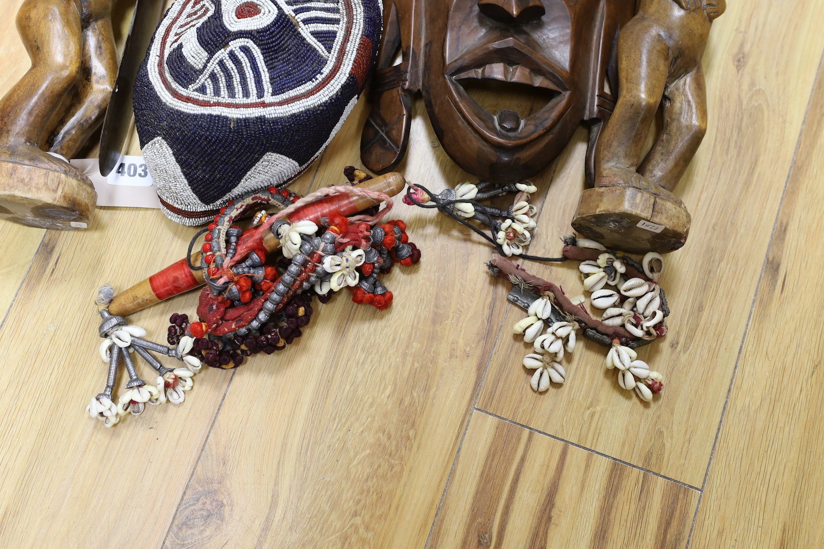 A group of African hardwood carvings, shell and beadwork including a cap